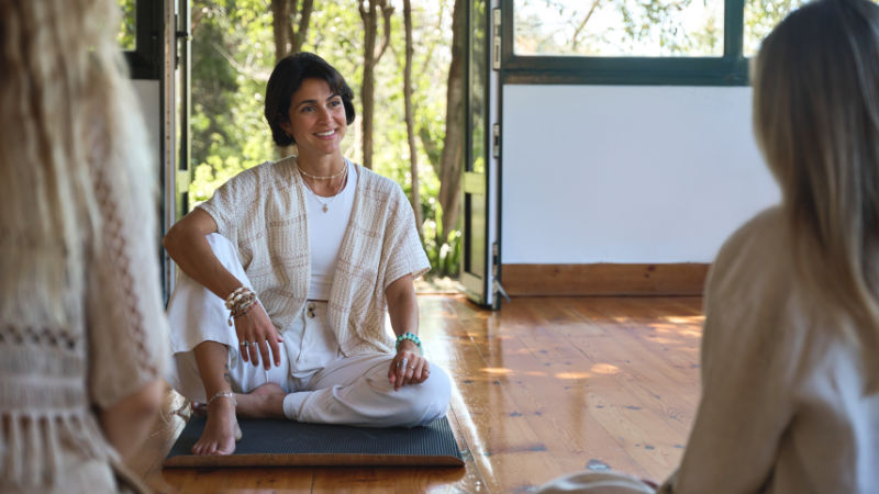 Young happy smiling Hispanic woman yoga coach training group class yoga meditation session sitting in yoga pose in studio talking to community people during retreat mind body health therapy