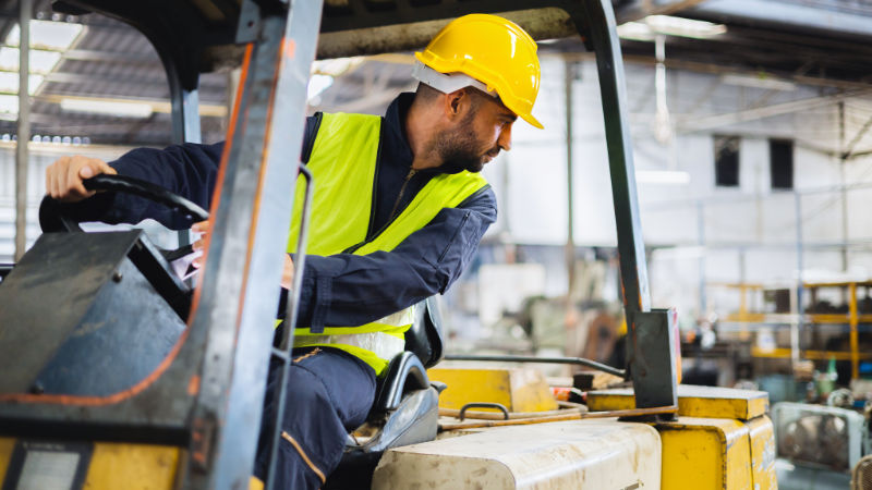 worker wearing helmet with driving forklift backwards in warehouse